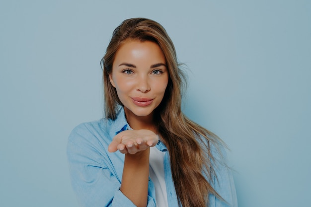 Woman blowing air kiss on light blue background