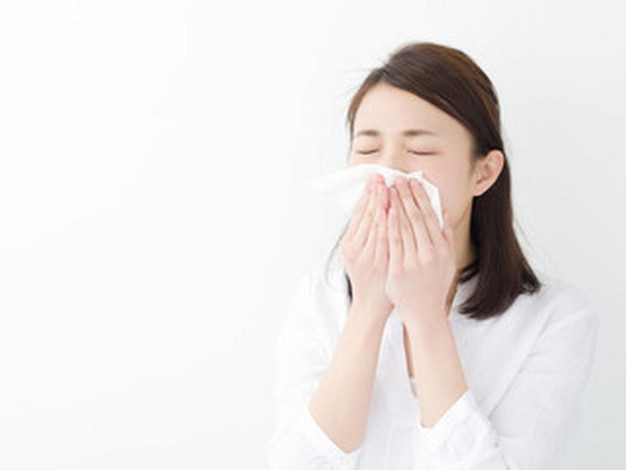 手にティッシュを持って鼻を吹く女性