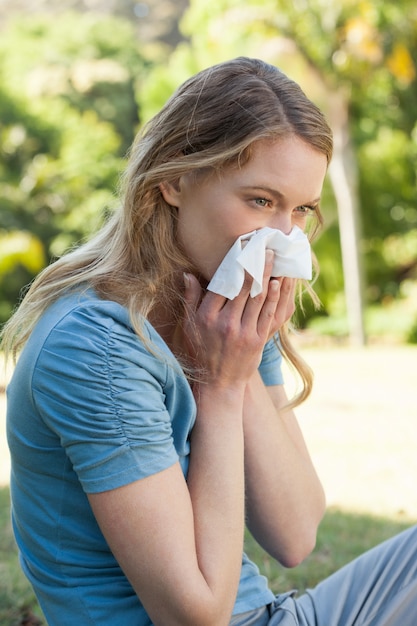 Woman blowing nose with tissue paper at park