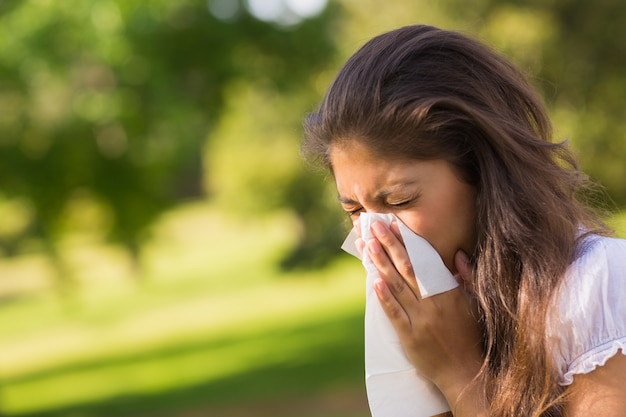 Photo woman blowing nose with tissue paper at park