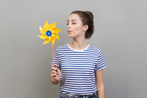 Woman blowing at paper windmill playing with pinwheel toy on stick