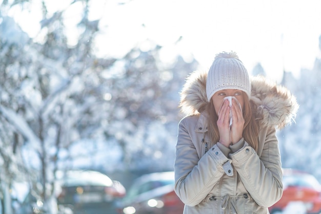 バックグラウンドで雪に覆われた山と寒い冬にティッシュを吹く女