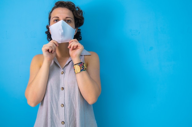 Woman on blue background preparing to take off her mask after
the pandemic with copy space