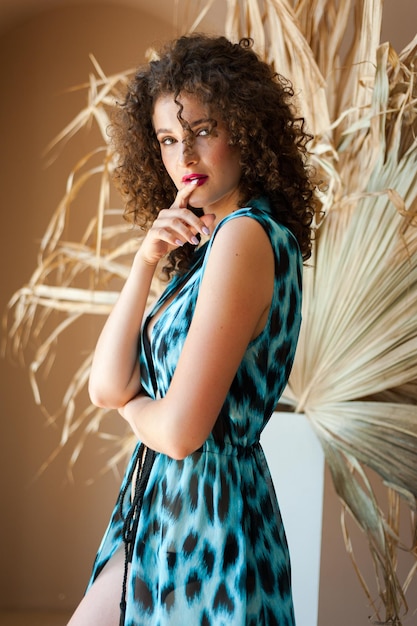 A woman in a blue and black dress stands in front of a plant