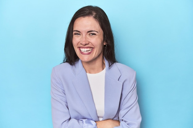 Woman in blue blazer on blue background laughing and having fun