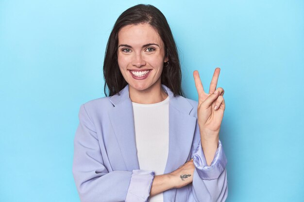 Woman in blue blazer on blue background showing number two with fingers