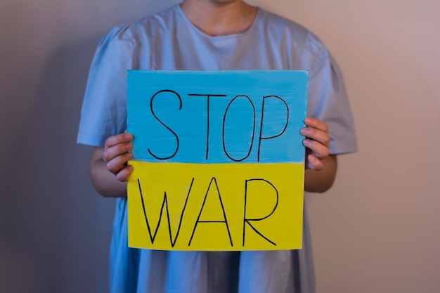 Woman in a blue dress holding a poster on an antiwar theme in her hands Ukrainian flag