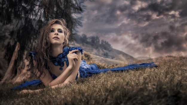 a woman in a blue dress is laying in the grass with a sky behind her