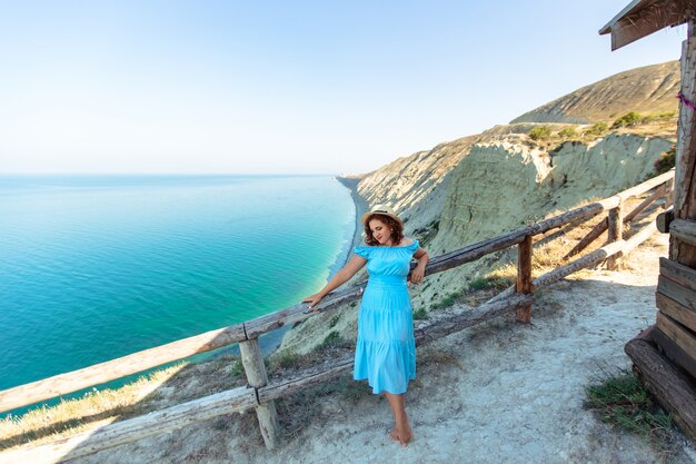 Женщина в синем платье на скалистом берегу моря
