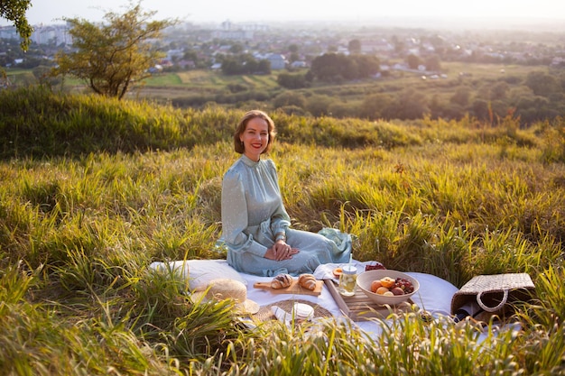 A woman in blue dress sits on a picnic in a park with panoramic view