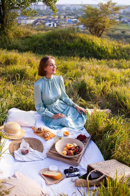 A woman in blue dress sits on a picnic in a park with panoramic view
