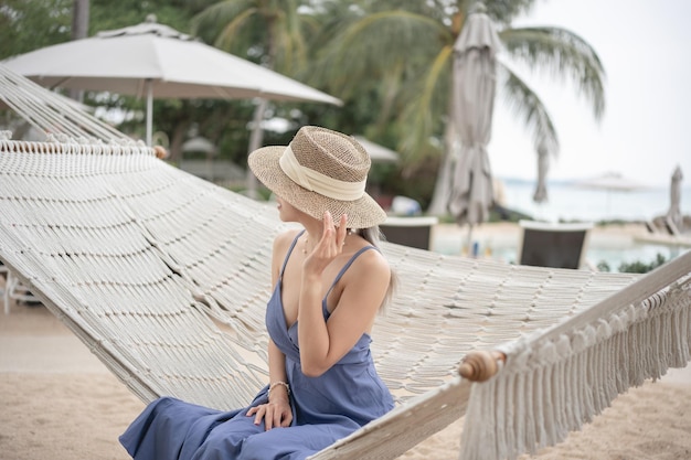 Woman in blue dress and straw hat relaxing in a hammock by the beach