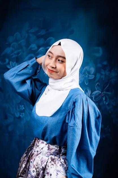 A woman in a blue dress and a white scarf is posing for a photo.