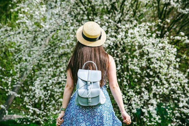 Photo woman in blue dress with hat in spring day looking at blooming bushes