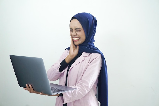 A woman in a blue hijab holds a laptop in her hands.