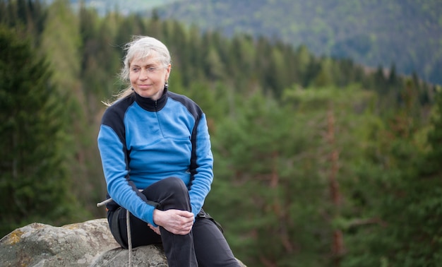 Woman in a blue jacket sit and relax on the peak of rock