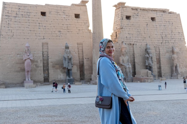 A woman in a blue jacket and sunglasses stands in front of a the Karnak temple of Luxor Egypt