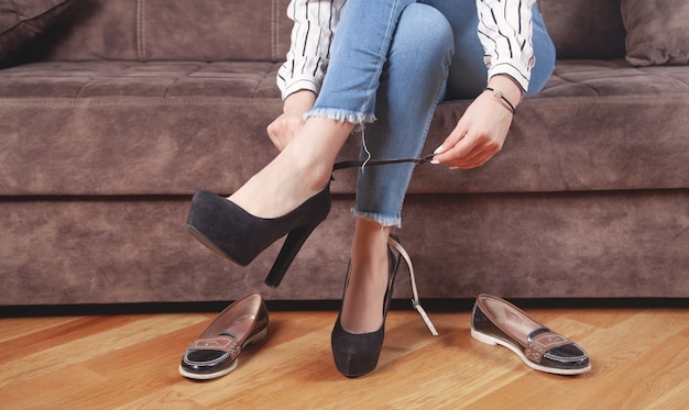 Photo woman in blue jeans choosing and trying shoes at home.