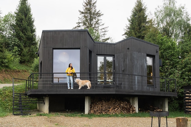 Foto donna e jeans blu e cane golden retriever vicino alla moderna cabina in legno in stile scandinavo s