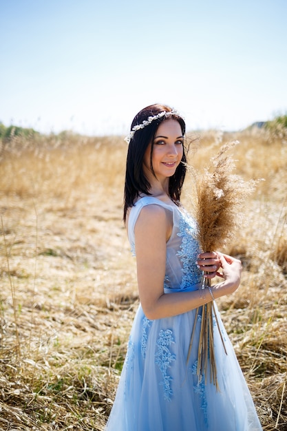 Woman in a blue long dress in the reeds. Fashion portrait with dried flowers