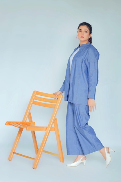 A woman in a blue outfit stands next to a wooden chair.