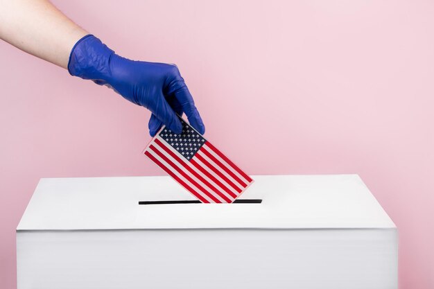 Woman in blue protective gloves puts the usa flag in a voting box elections and coronavirus concept