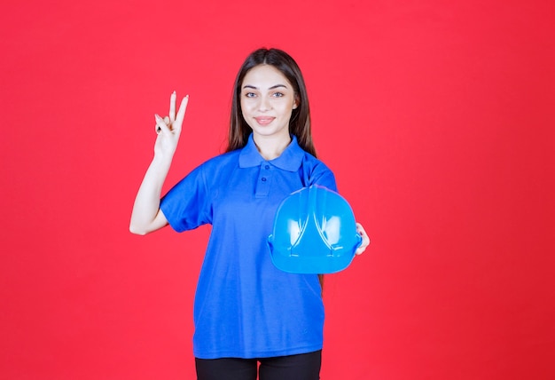 woman in blue shirt holding a blue helmet and showing positive hand sign. 