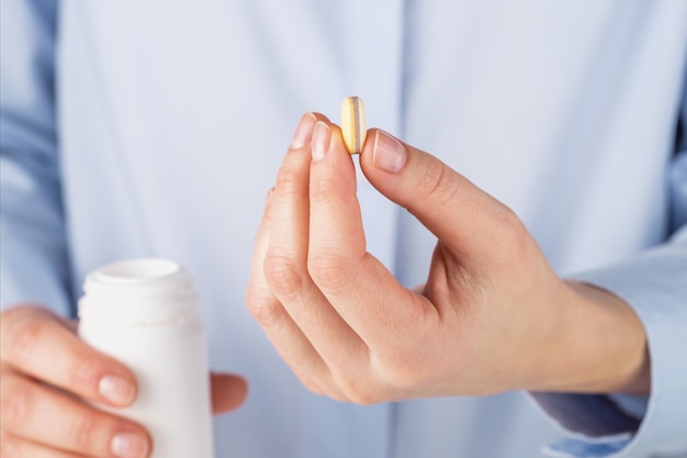 A woman in a blue shirt holds a pill in her hands, close-up.