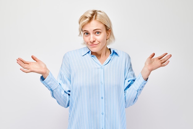 Woman in blue shirt shrugging with uncertain playful expression on a light background