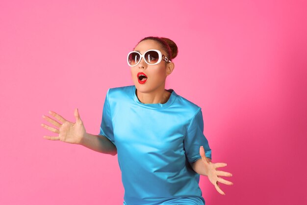 woman in blue silk dress and white sunglasses ot the pink background