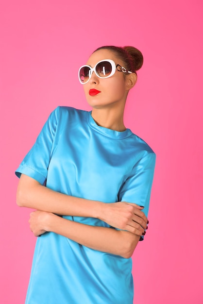 woman in blue silk dress and white sunglasses ot the pink background