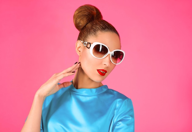 woman in blue silk dress and white sunglasses ot the pink background