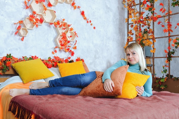 женщина в синем свитере сидит в уютном доме с осенними украшениями, оранжевыми тыквами. Осень.