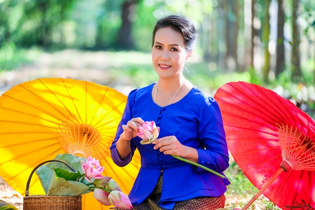 A woman in a blue Thai dress is holding a beautiful lotus flower.