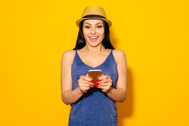 A woman in a blue top and a blue top is holding a phone and texting on a yellow background.