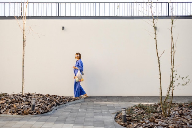 青い服を着た女性が新鮮な食べ物で満たされたメッシュバッグを持って歩いています