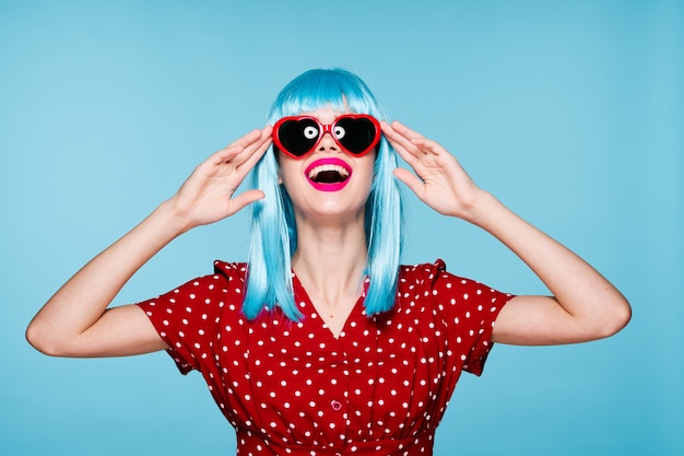 Photo woman in a blue wig on a blue background in glasses with an open mouth