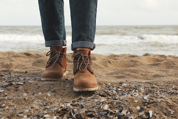 woman in boots and jeans standing on sandy beach