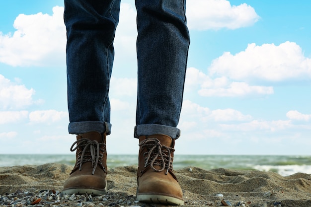 woman in boots and jeans standing on sandy beach