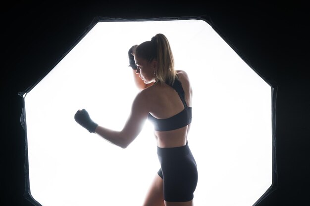 Женщина-боксер в перчатках тренируется на черном красно-желтом фоне