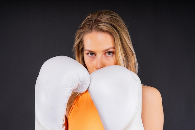 Woman boxer in gloves training on yellow and dark studio background