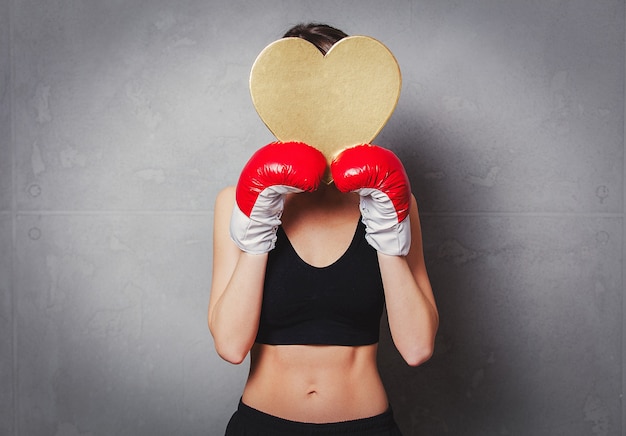 Photo woman in boxing gloves with heart shape gift box in hands