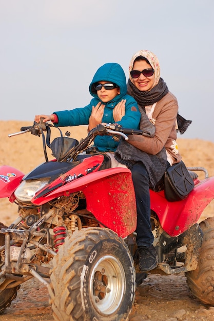 砂漠で四輪バイクに乗る女性と少年。