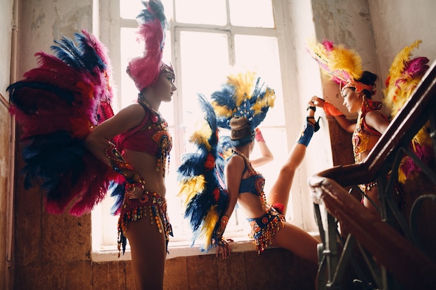 Woman in brazilian samba carnival costume with colorful feathers plumage relax in old entrance with big window.