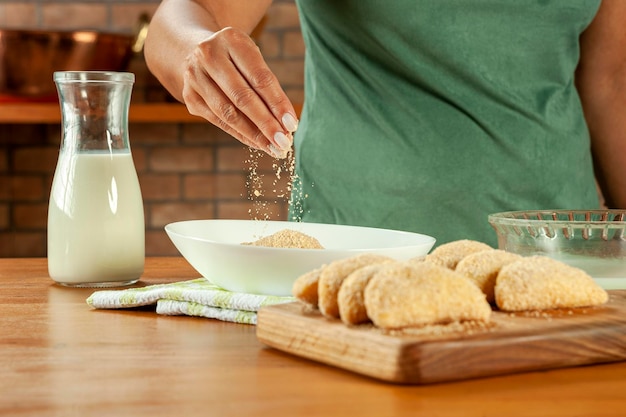 Woman breading brazilian meat stuffed croquette risolis de carne on a wooden table Top view