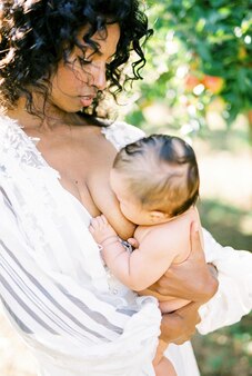 Donna che allatta al seno il suo neonato in giardino