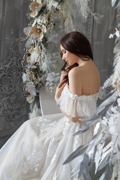 Woman bride in a white dress swings on a round swing made of\
white flowers and feathers a romantic image of a woman with a\
tattoo on her arm wedding