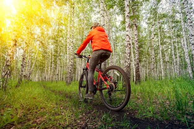 Woman in bright orange jacket riding bike on mountain top
forest trail