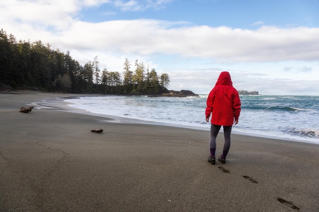 Woman in a bright red jacket is enjoying the scenery of the sandy beach