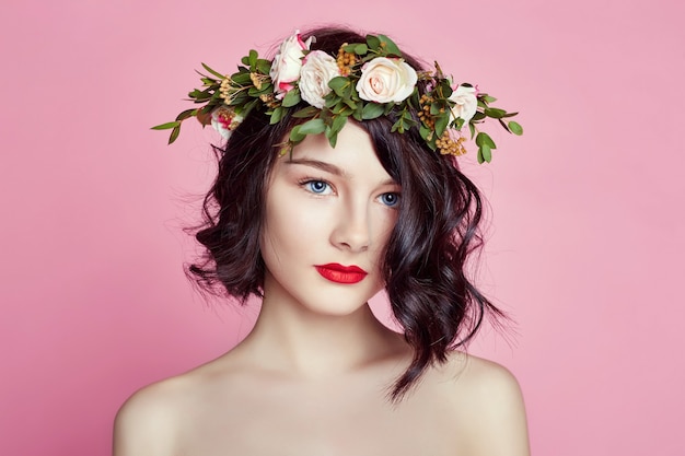 Woman bright summer look beautiful clothes. Flowers wreath on head. Brunette girl posing and smiling on bright pink background. Lady with flowers